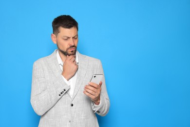 Pensive man looking at smartphone on light blue background. Space for text