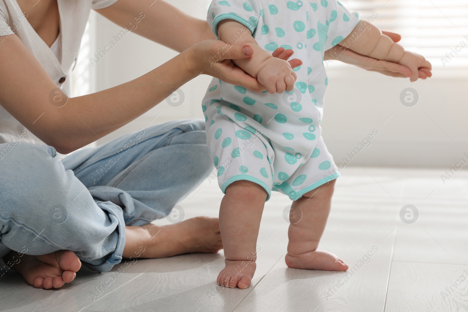 Photo of Mother supporting her baby daughter while she learning to walk at home, closeup