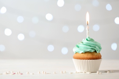 Photo of Delicious birthday cupcake with burning candle and space for text on blurred lights background