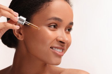 Photo of Smiling woman applying serum onto her face on white background, closeup