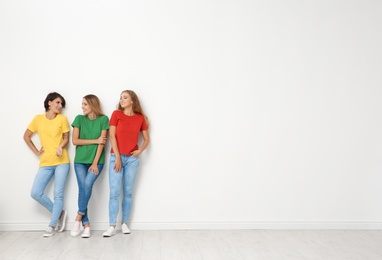 Photo of Group of young women in jeans and colorful t-shirts near light wall