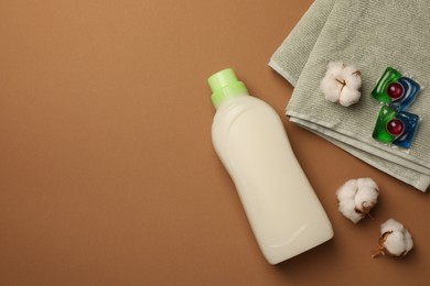 Photo of Flat lay composition with bottle of fabric softener and laundry detergent pods on brown background, space for text