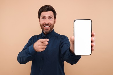 Photo of Handsome man showing smartphone in hand and pointing at it on light brown background