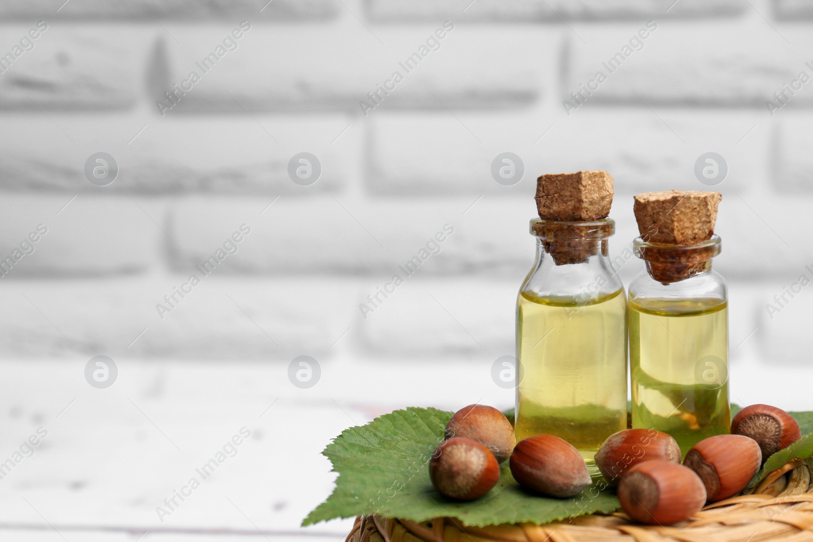 Photo of Bottles of hazelnut essential oil and nuts on wicker box. Space for text