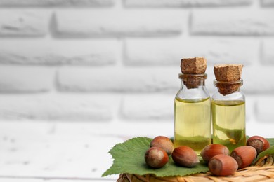 Bottles of hazelnut essential oil and nuts on wicker box. Space for text