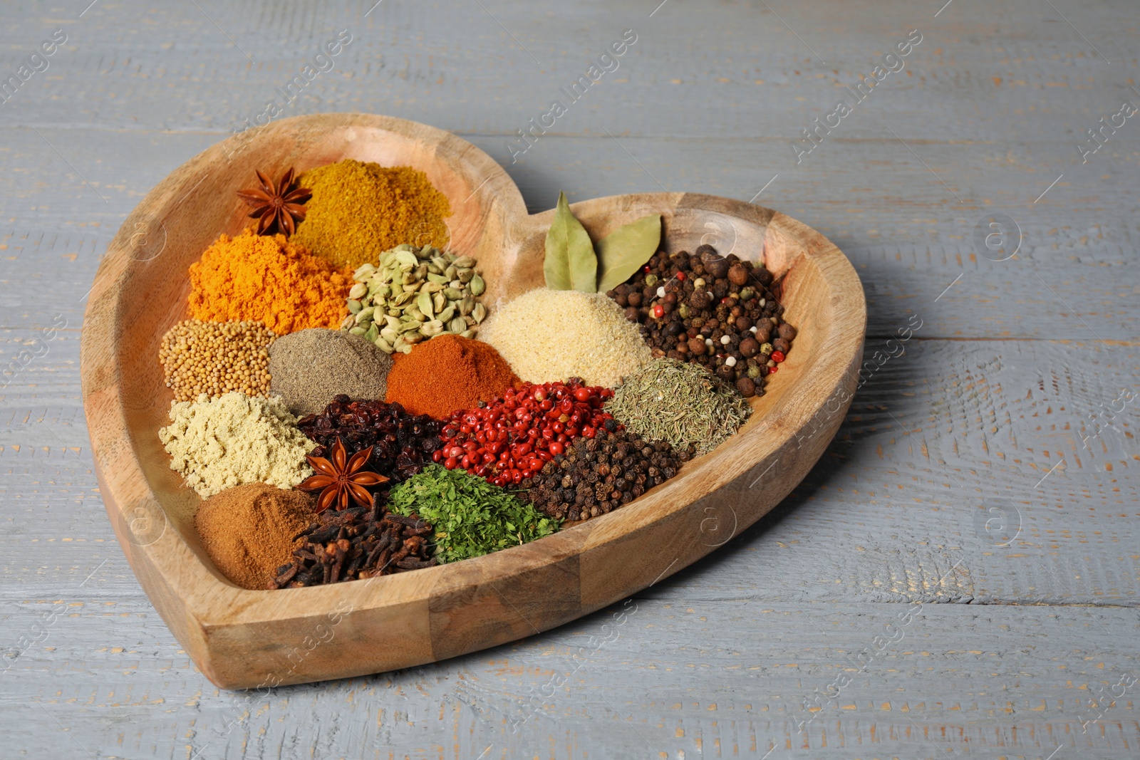 Photo of Heart shaped plate with different spices on grey wooden table