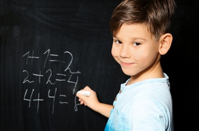 Photo of Little child with chalk doing math at blackboard