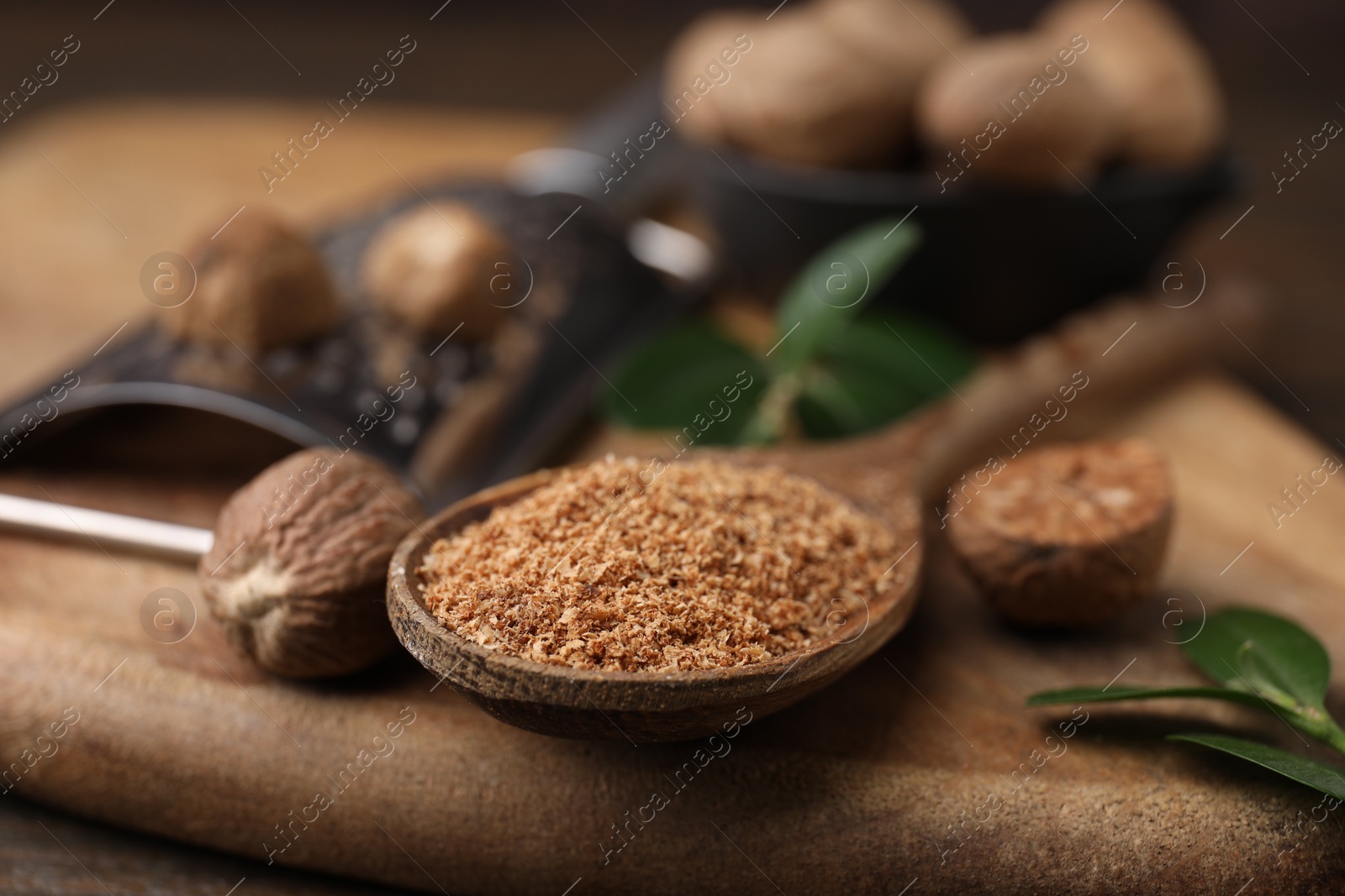 Photo of Spoon with grated nutmeg on wooden board, closeup