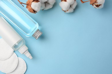 Photo of Bottles of makeup removers, cotton flowers and pads, on light blue background, flat lay. Space for text