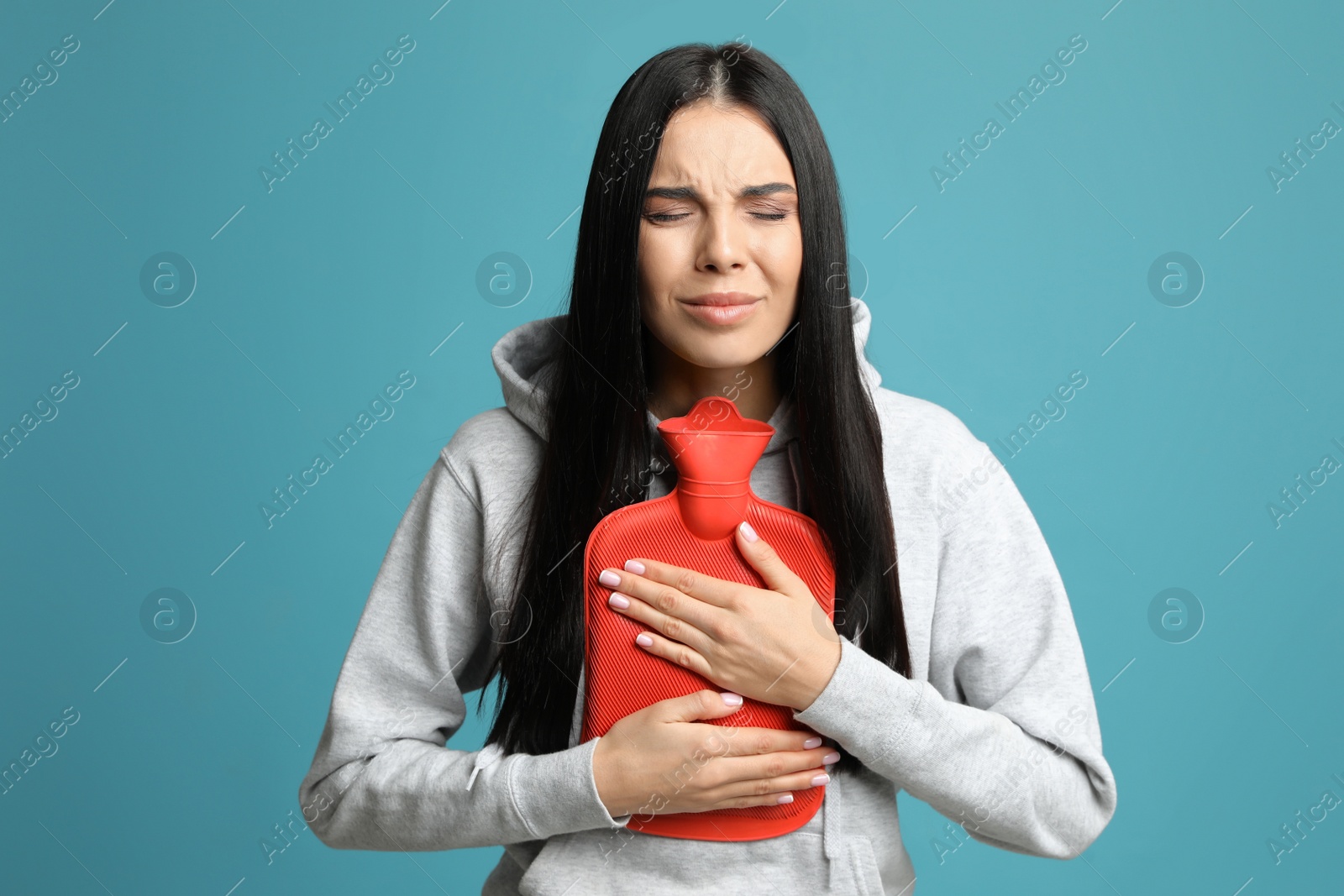 Photo of Woman using hot water bottle to relieve pain on light blue background