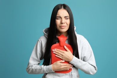 Photo of Woman using hot water bottle to relieve pain on light blue background