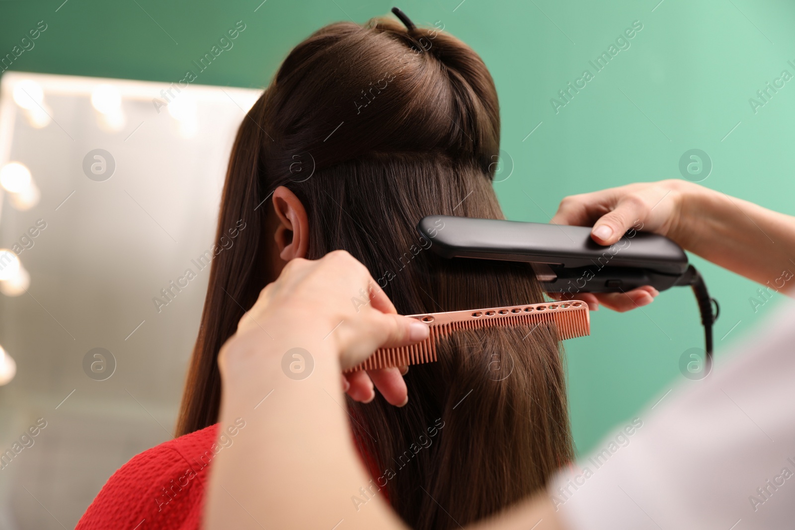 Photo of Stylist straightening woman's hair with flat iron in salon