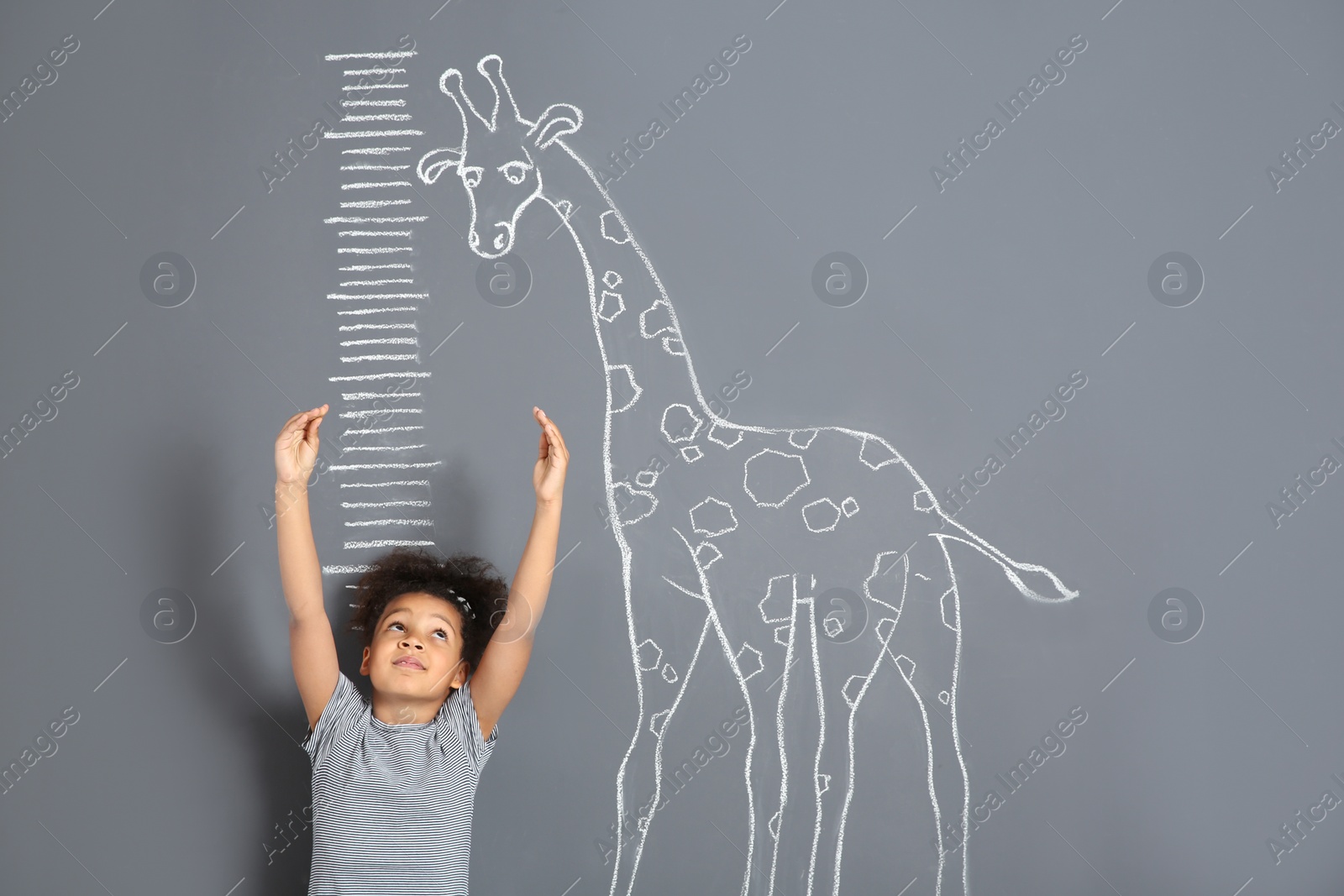 Photo of African-American child measuring height near chalk giraffe drawing on grey background