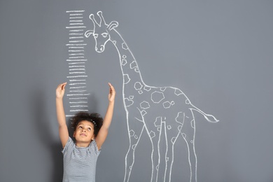 African-American child measuring height near chalk giraffe drawing on grey background