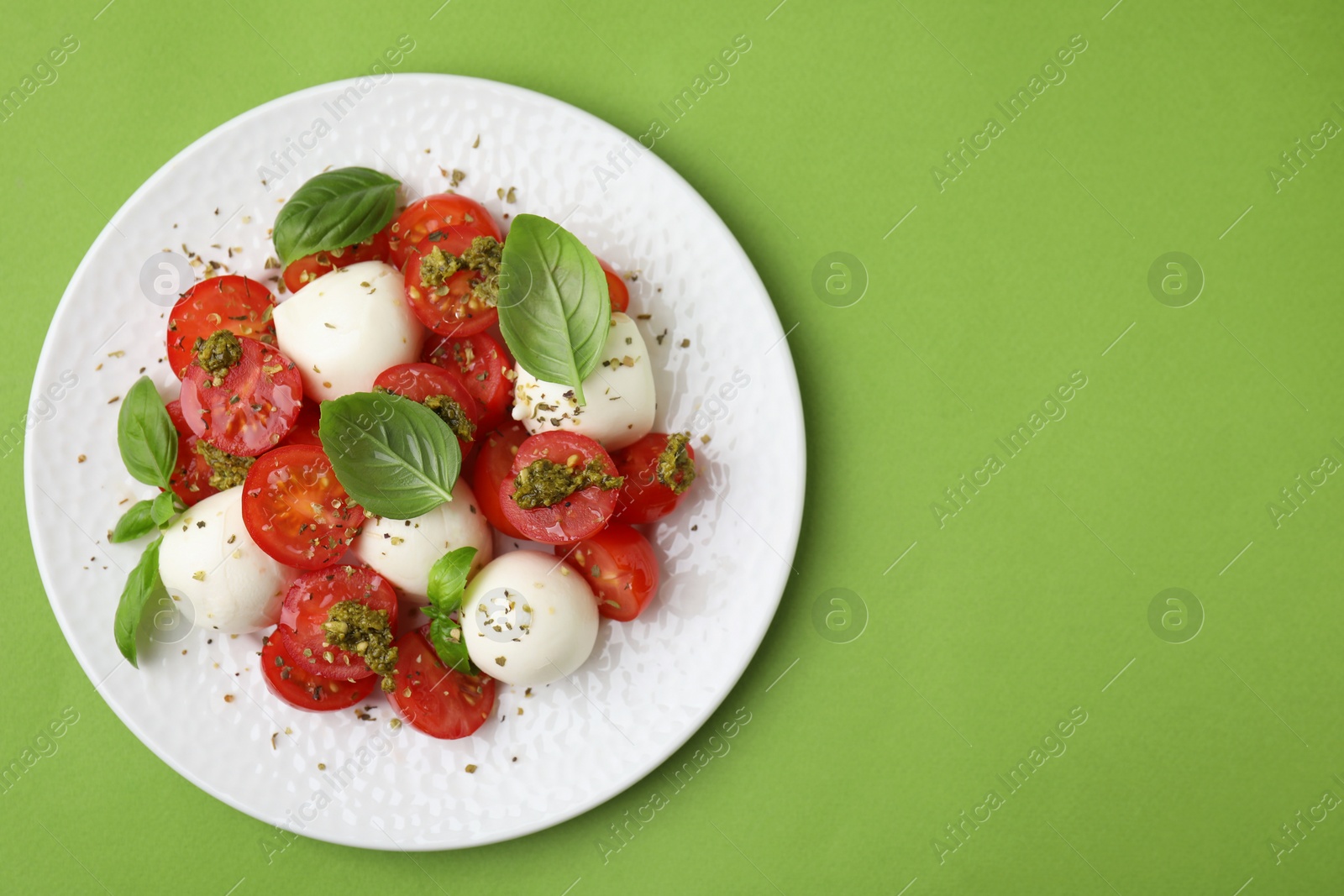 Photo of Tasty salad Caprese with tomatoes, mozzarella balls and basil on green background, top view. Space for text