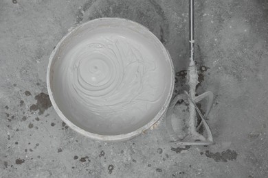 Bucket with plaster and power mixer on concrete floor, flat lay
