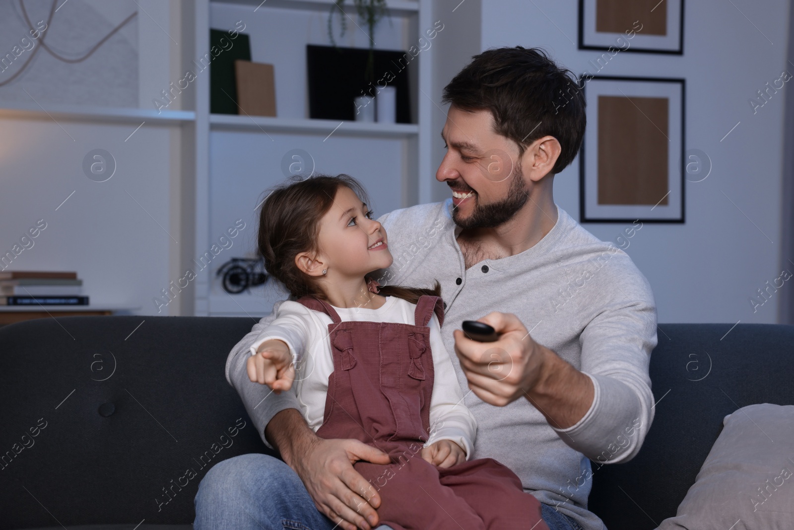 Photo of Father and daughter spending time near TV at home. Happy man holding remote control