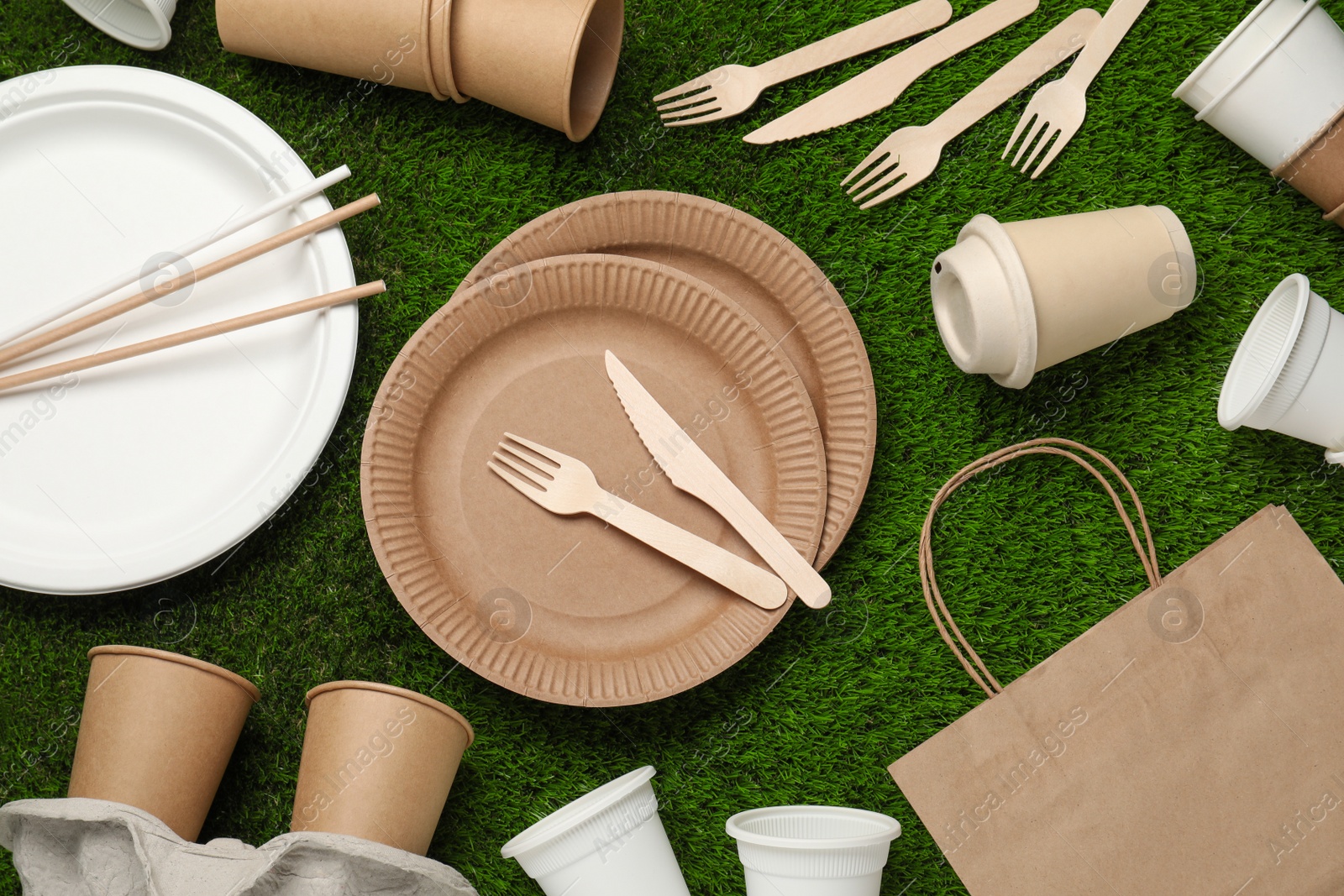 Photo of Eco disposable tableware on green artificial grass, flat lay