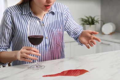 Photo of Embarrassed woman with wine stain on her shirt and spilled wine at white marble table indoors, closeup
