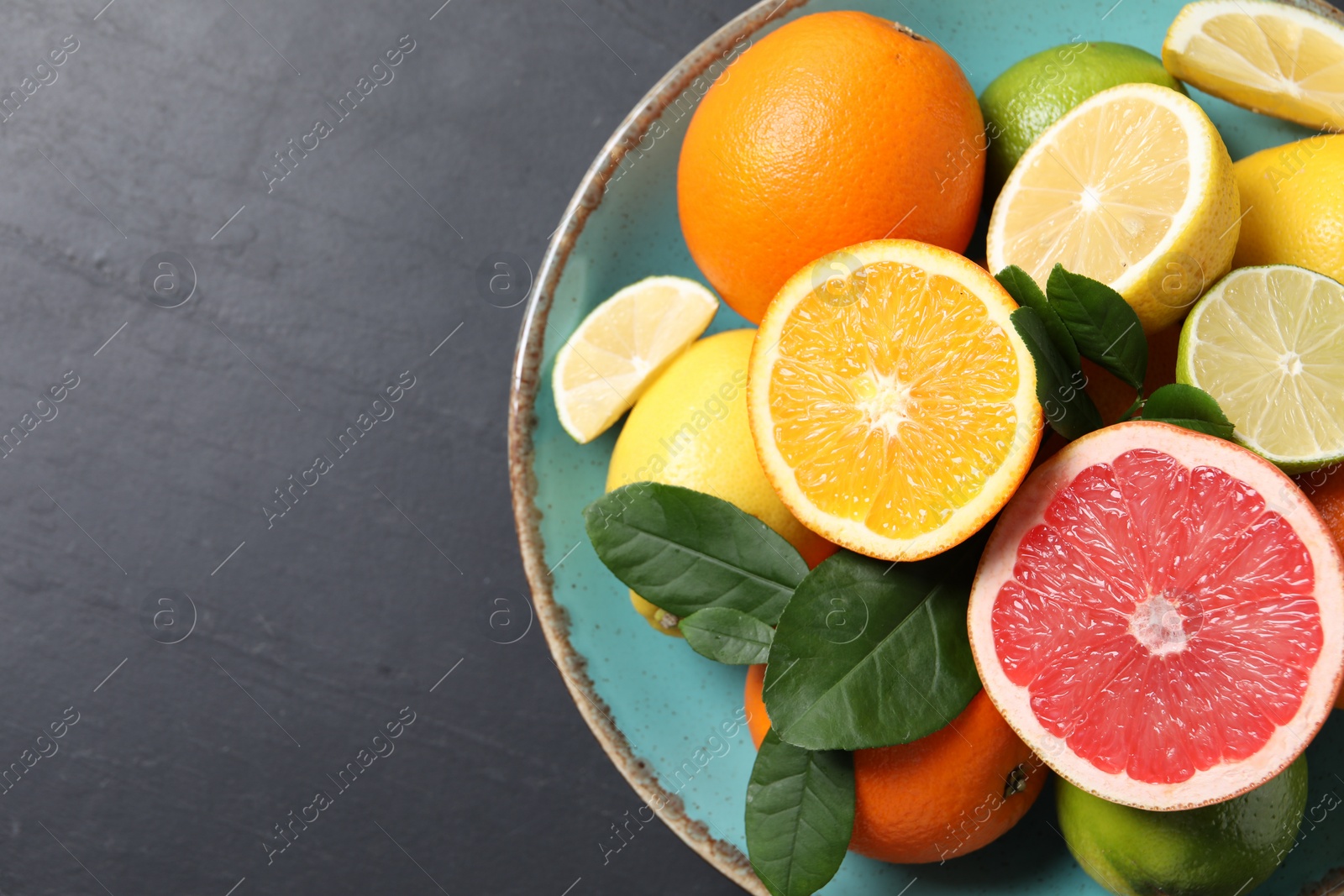 Photo of Different cut and whole citrus fruits on black table, top view. Space for text