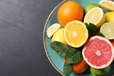 Different cut and whole citrus fruits on black table, top view. Space for text