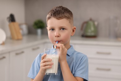 Cute boy drinking fresh milk from glass indoors