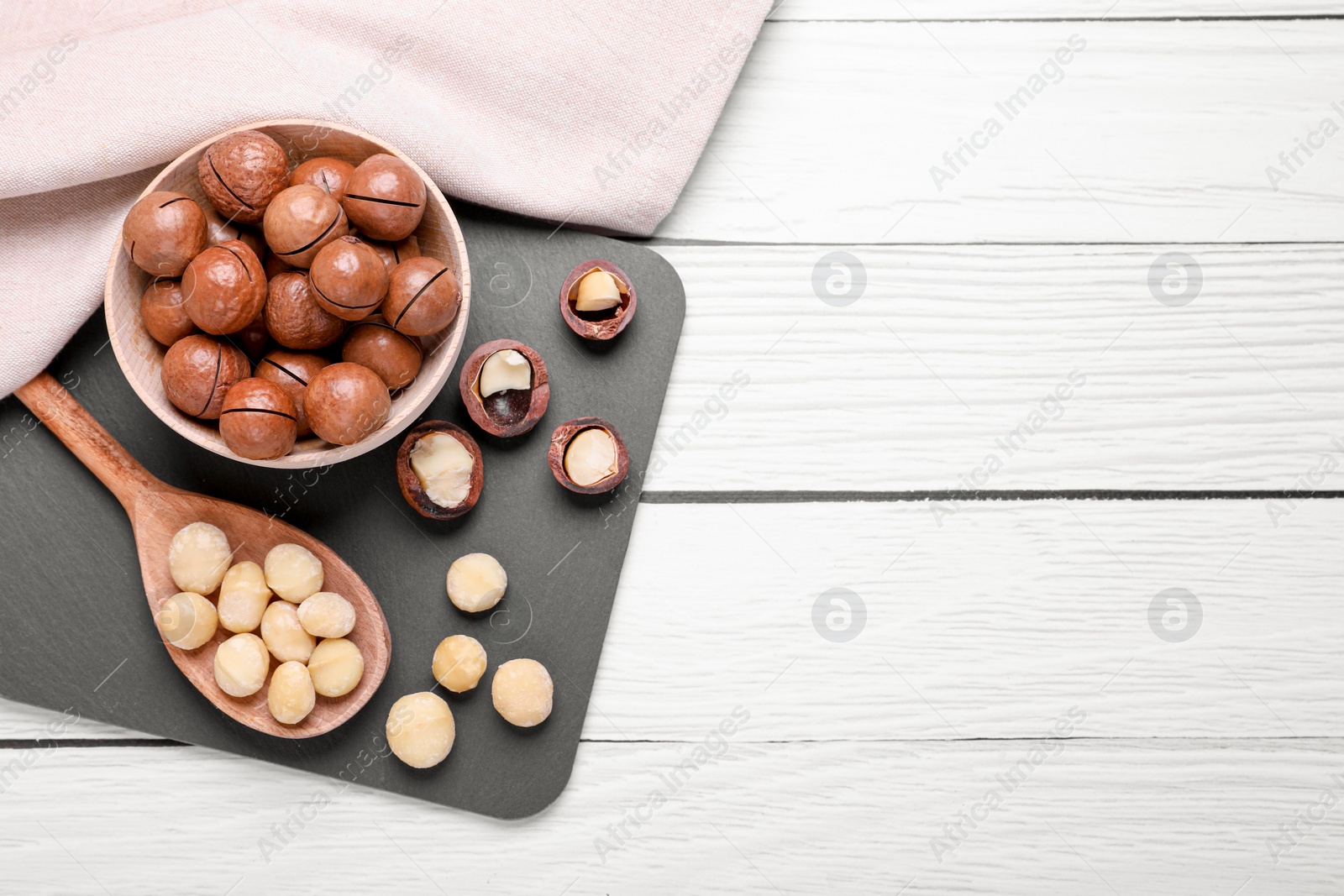 Photo of Delicious organic Macadamia nuts on white wooden table, top view. Space for text