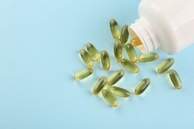 Photo of Bottle and vitamin capsules on light blue background, top view. Space for text