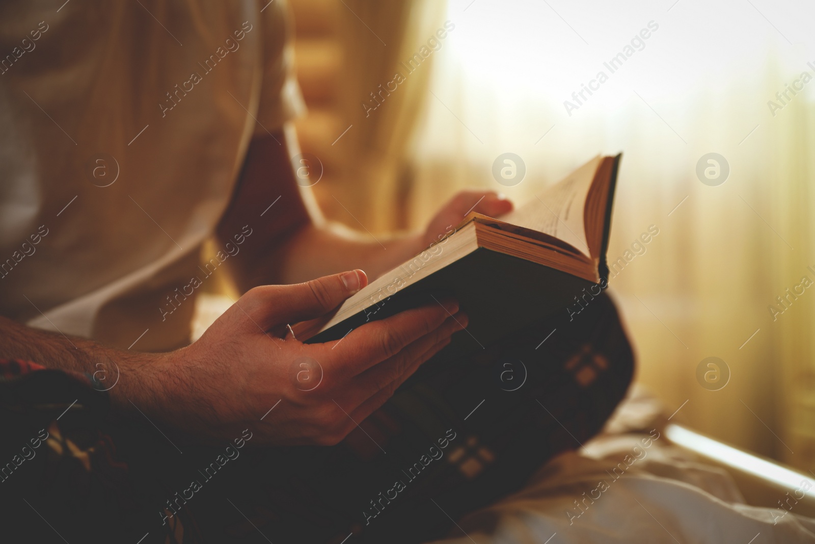 Photo of Young man reading book on bed at home, closeup