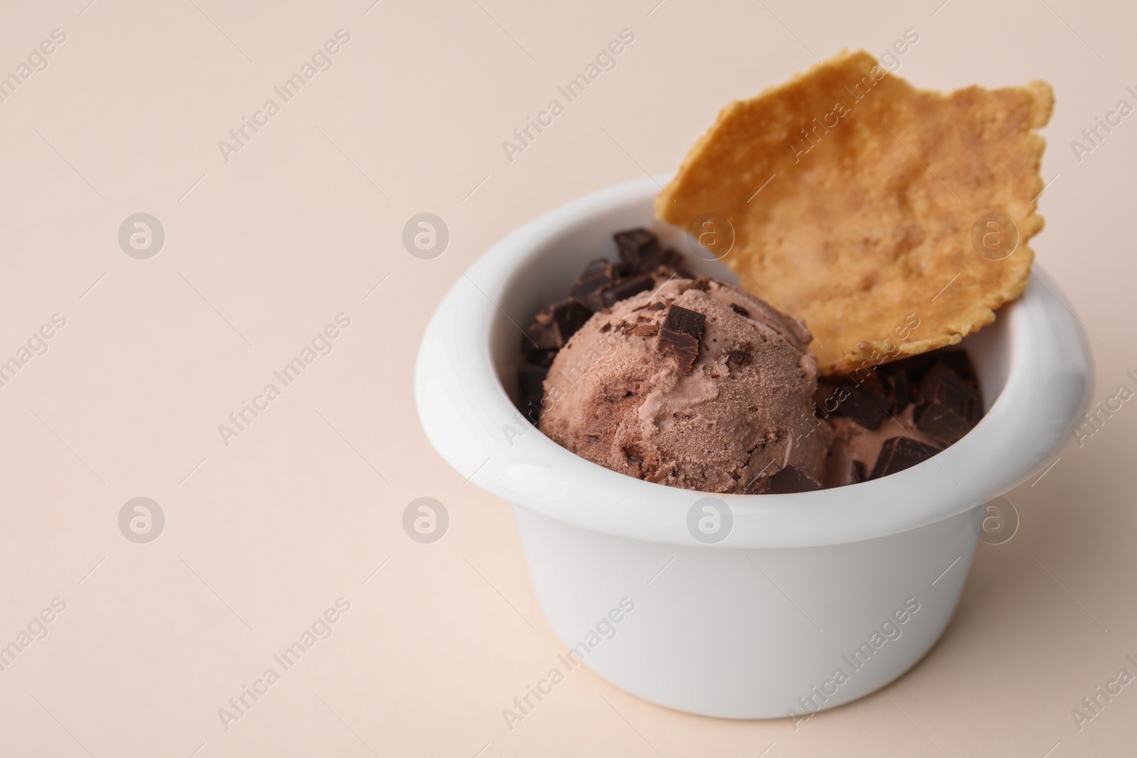 Photo of Tasty chocolate ice cream and piece of waffle cone in bowl on beige background, closeup. Space for text