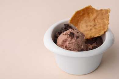 Tasty chocolate ice cream and piece of waffle cone in bowl on beige background, closeup. Space for text