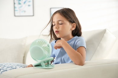 Little girl enjoying air flow from portable fan at home. Summer heat