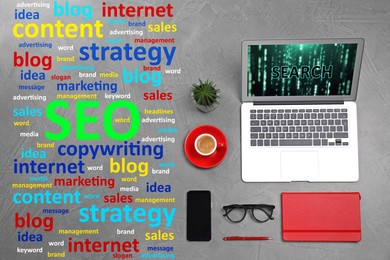 Image of Search engine optimization (SEO). Marketing terms, laptop and stationery on grey textured table, flat lay