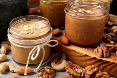 Photo of Tasty nut butters in jars and raw nuts on table, closeup