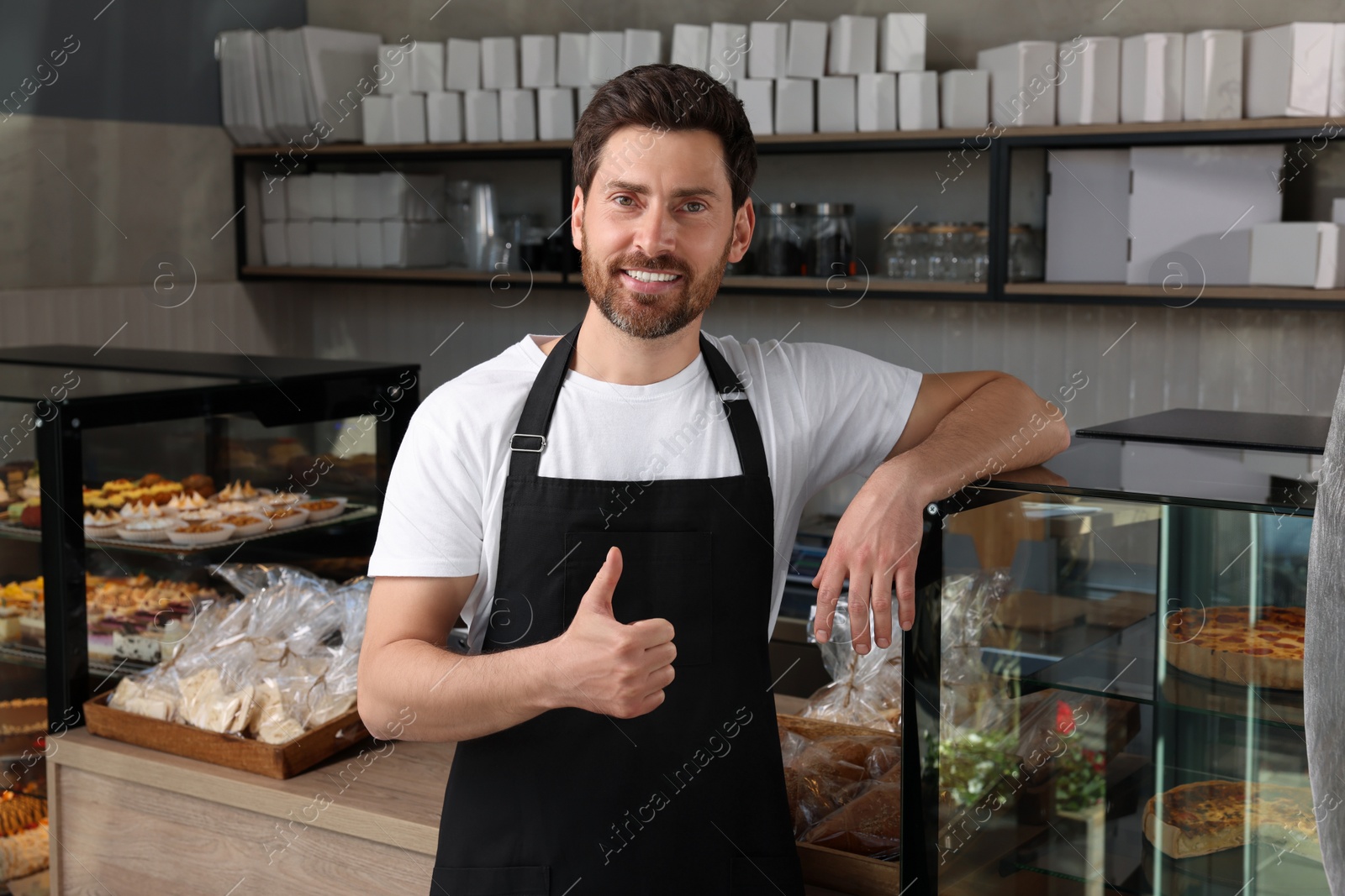 Photo of Happy seller showing thumb up near showcase in bakery shop