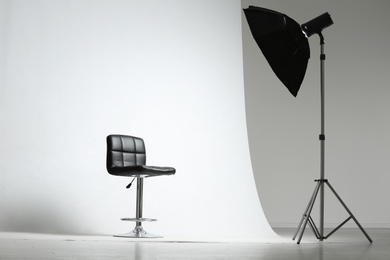Photo of Modern chair and professional lighting equipment in photo studio