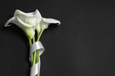 Photo of Beautiful calla lilies and white ribbon on black background, flat lay with space for text. Funeral symbol