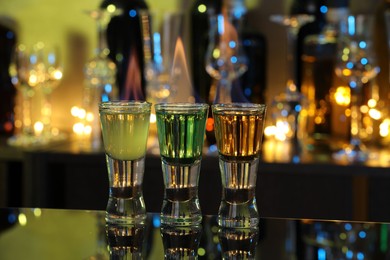 Photo of Flaming shooters in shot glasses on mirror surface against blurred background. Alcohol drink