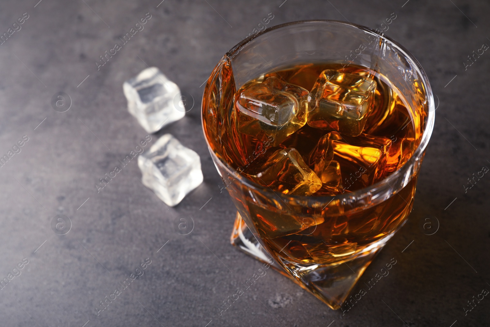 Photo of Golden whiskey in glass with ice cubes on table. Space for text