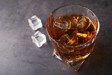 Golden whiskey in glass with ice cubes on table. Space for text