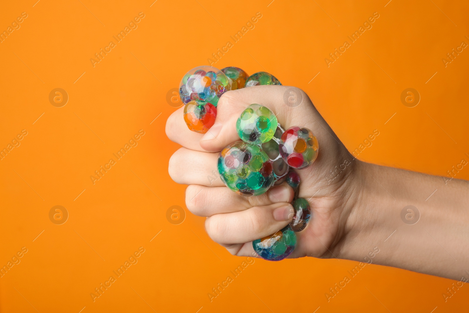 Photo of Woman squeezing colorful slime on orange background, closeup. Antistress toy