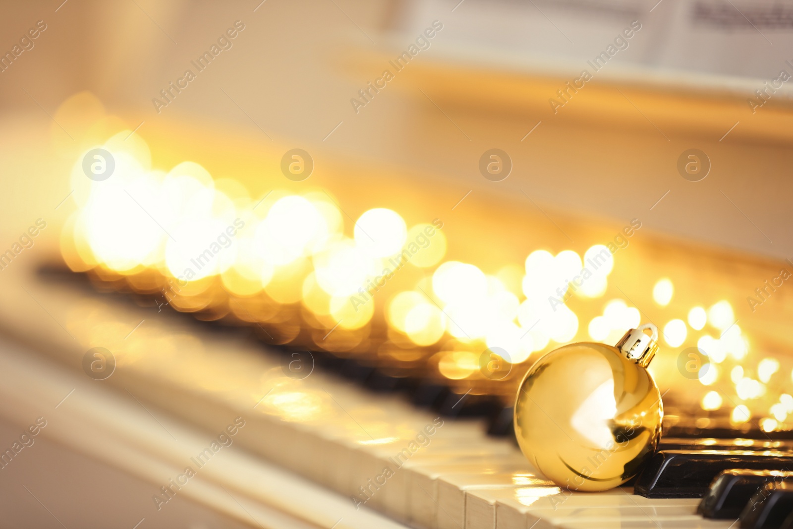 Photo of Beautiful golden bauble and fairy lights on piano keys, space for text. Christmas music