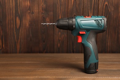 Modern electric power drill on wooden table, space for text