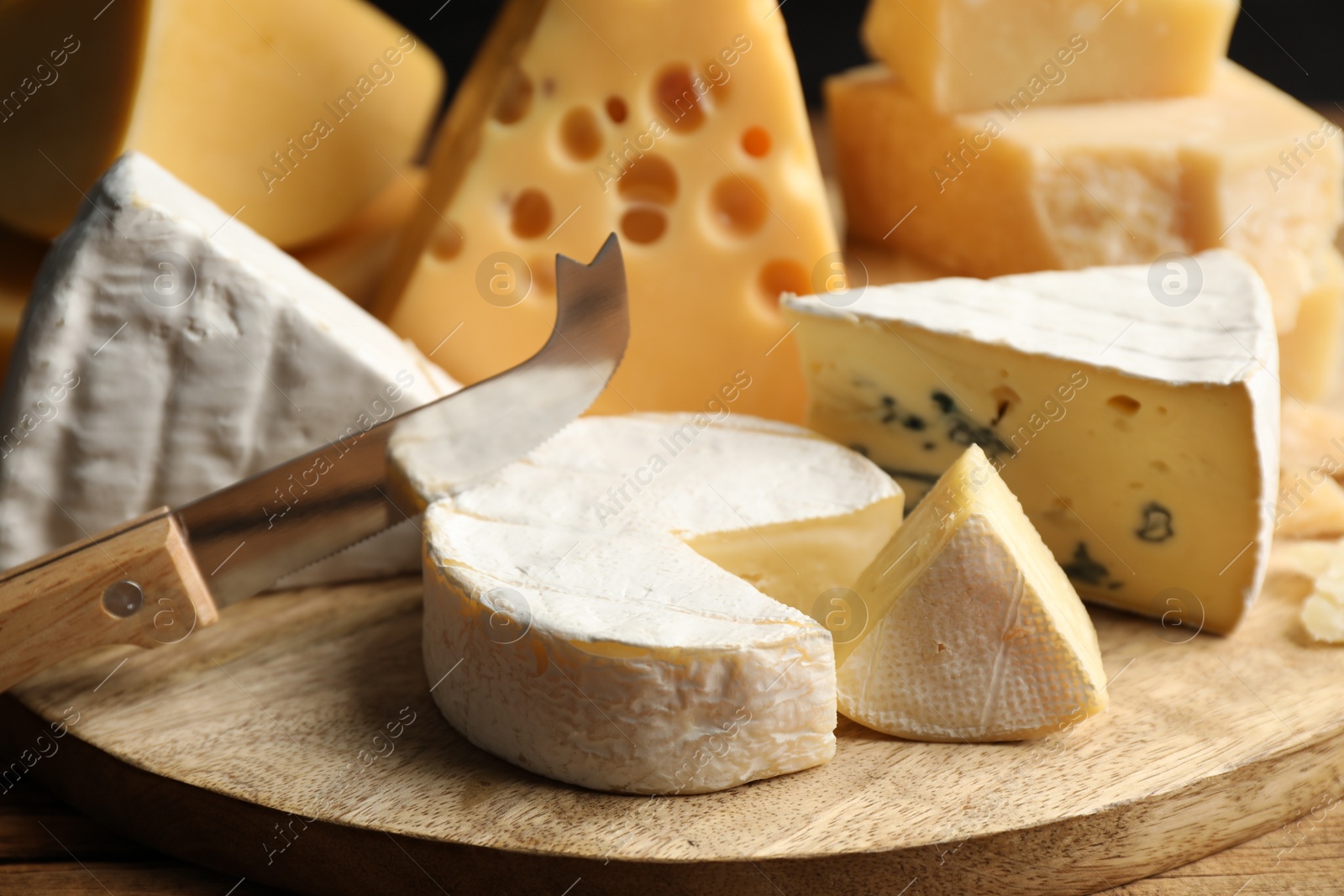 Photo of Different sorts of cheese and knife on wooden table, closeup