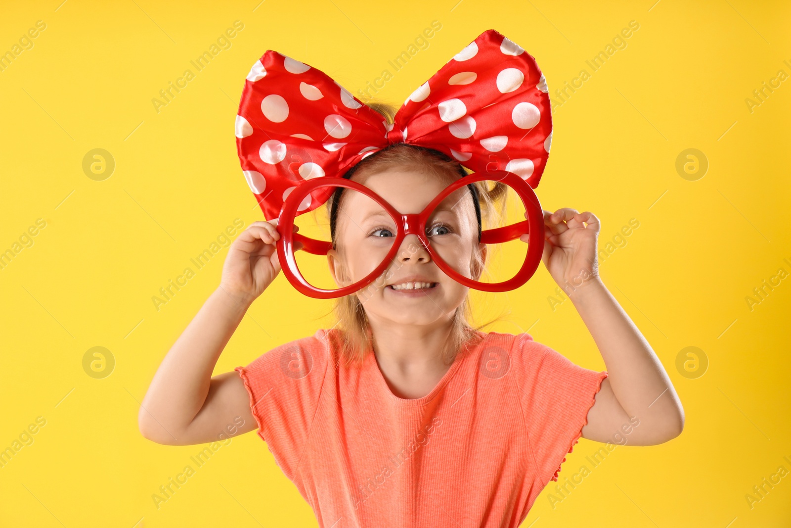 Photo of Little girl with large bow and funny glasses on yellow background. April fool's day