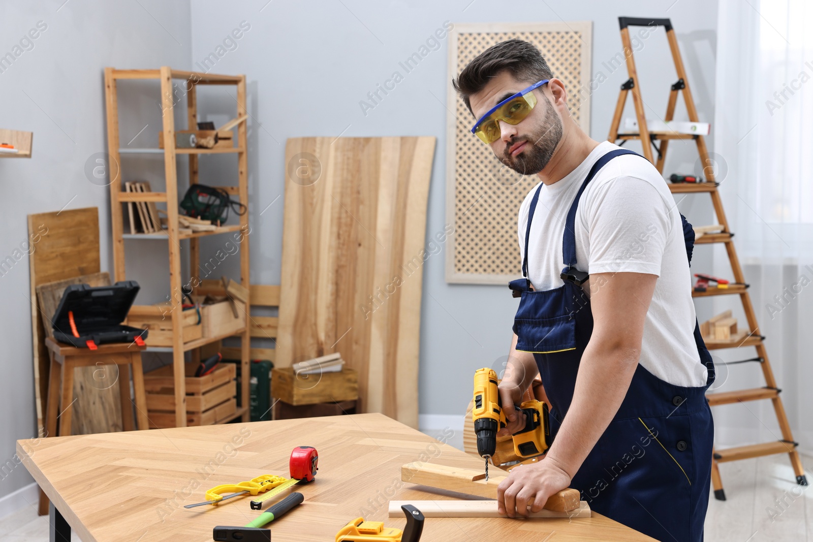 Photo of Young worker using electric drill at table in workshop