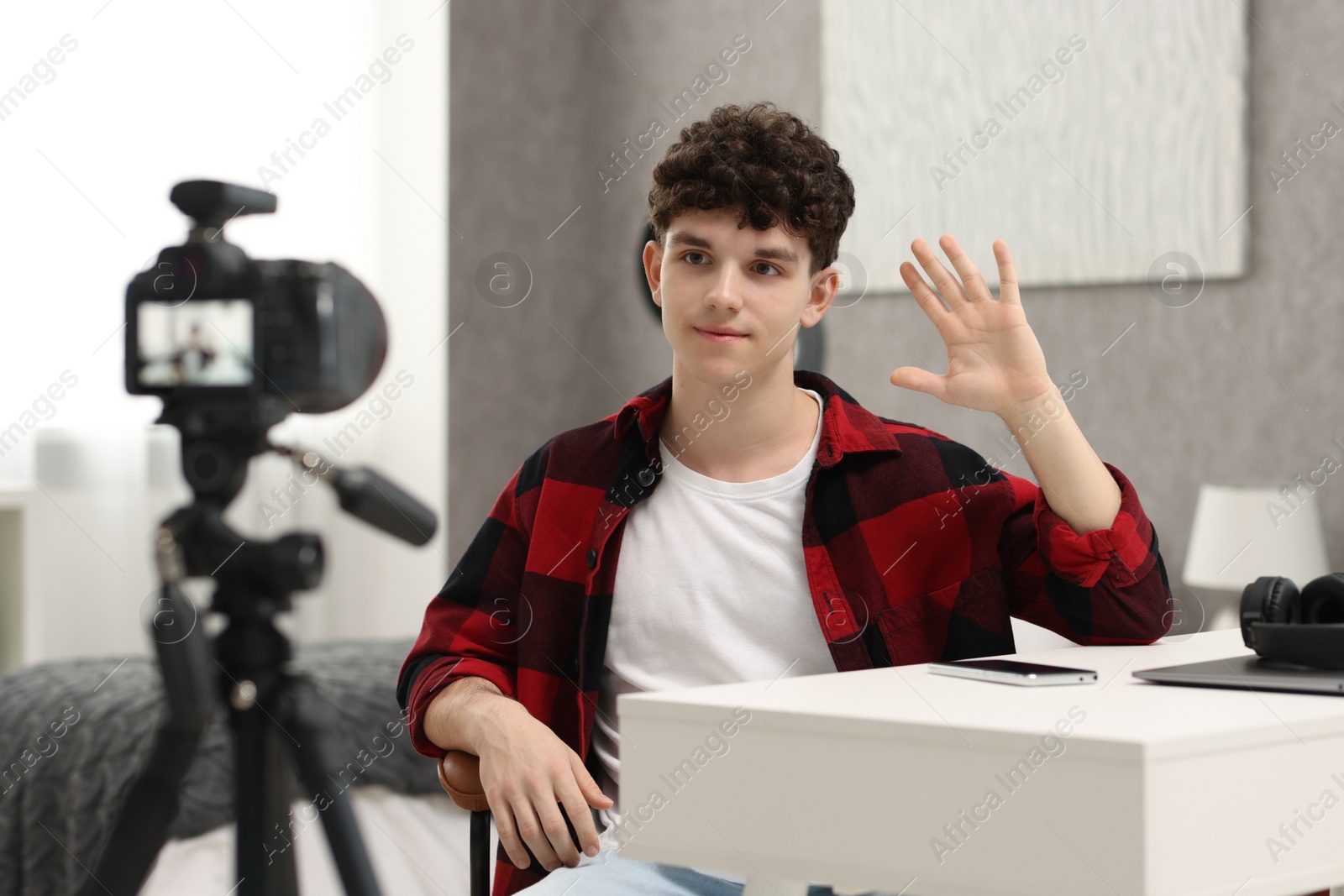 Photo of Teenage blogger waving hello to his subscribers while streaming at home