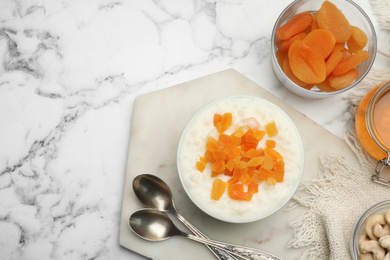 Photo of Delicious rice pudding with dried apricots on white marble table, flat lay. Space for text
