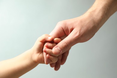 Photo of Father and child holding hands on light blue background, closeup