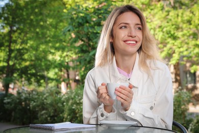 Photo of Happy young woman with cup of coffee enjoying early morning in outdoor cafe